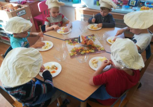 Dzieci przy stoliku kroją owoce.